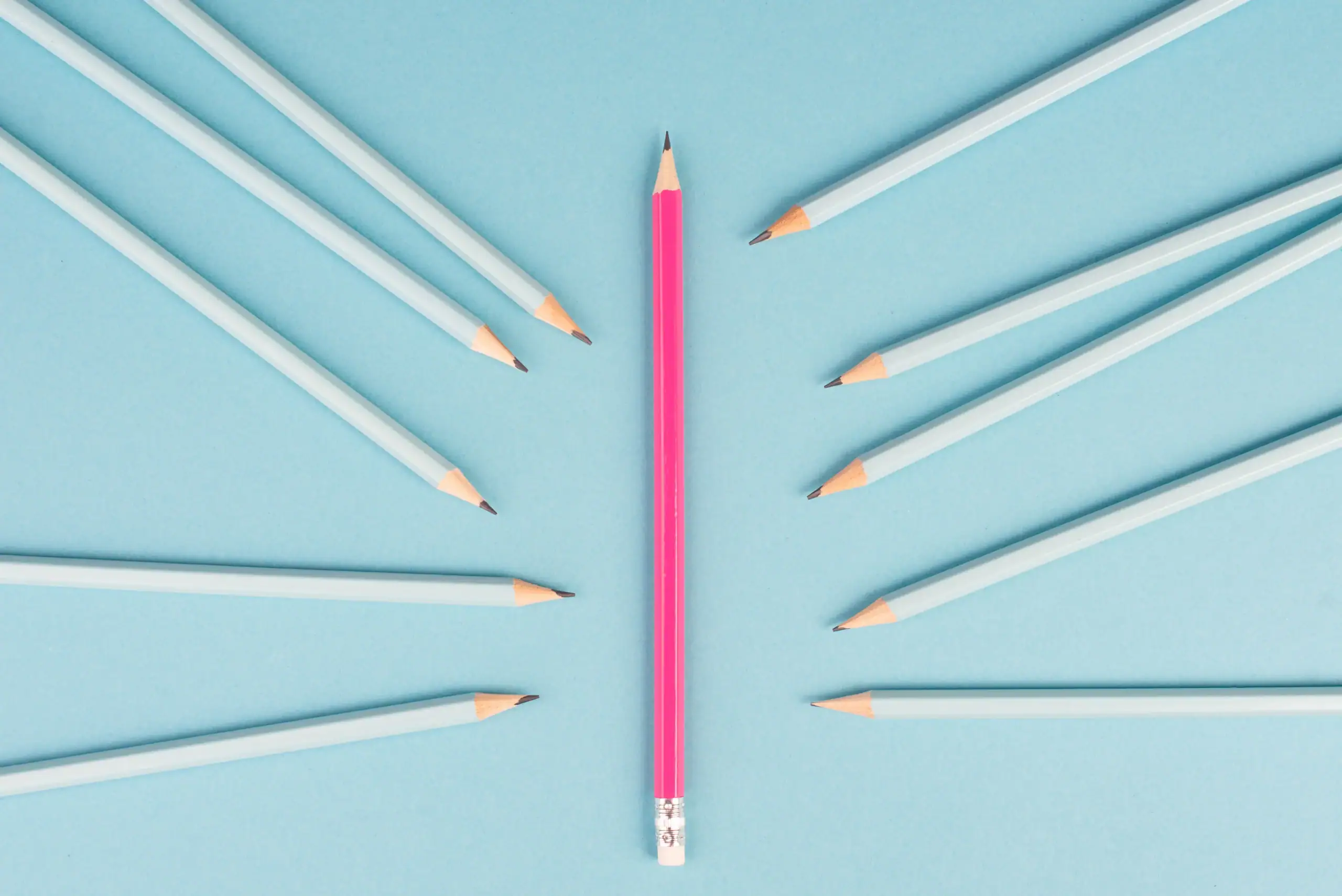 A single pink pencil stands upright in the center, surrounded by ten blue pencils pointing toward it on a light blue background, symbolizing focus and support—much like effective OCD therapy Texas and Minnesota can offer.
